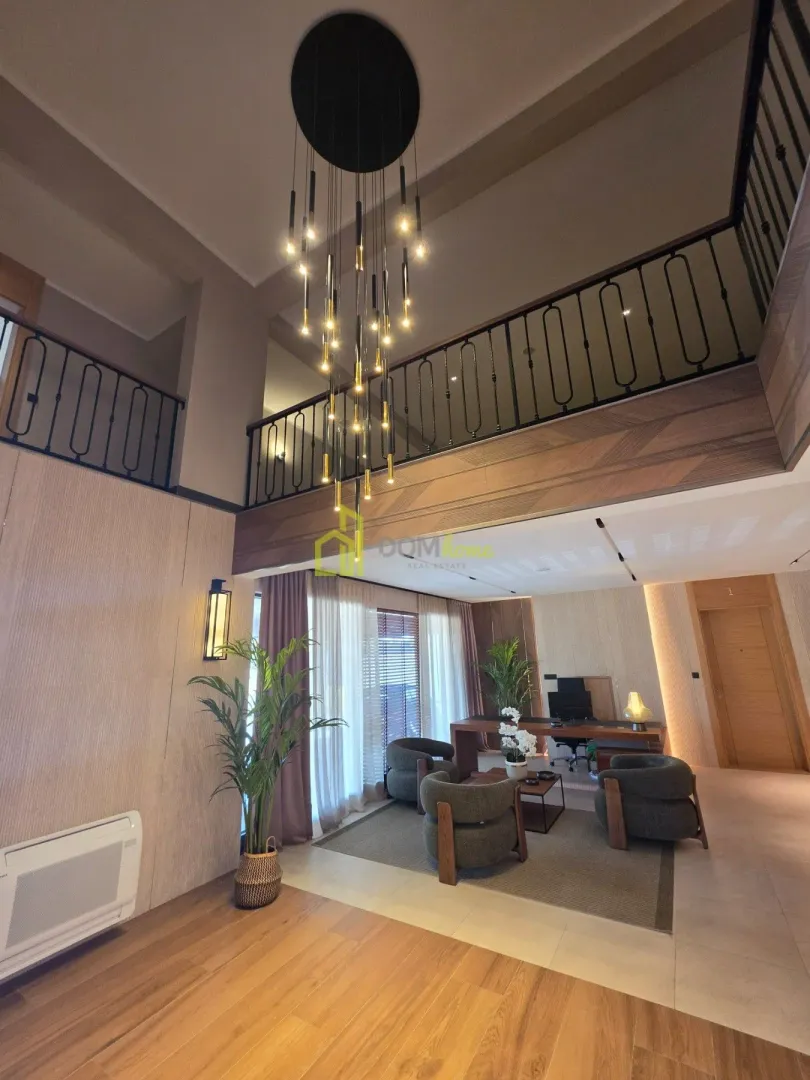 Spacious living room with high ceiling, gallery, and modern chandelier.