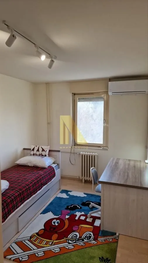Dečja soba sa krevetom, radnim stolom i tepihom sa motivom voza.
