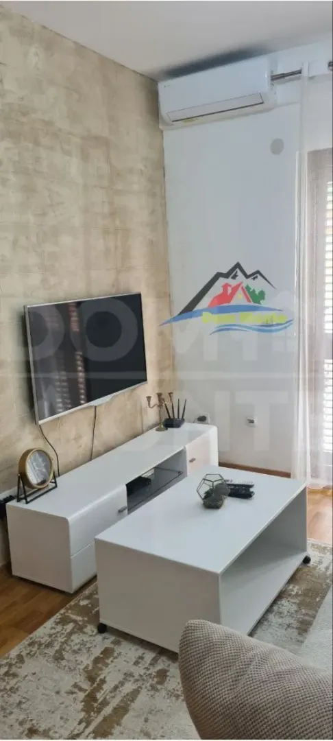 Dnevna soba sa garniturom, TV-om i bijelim komadnim namještajem.