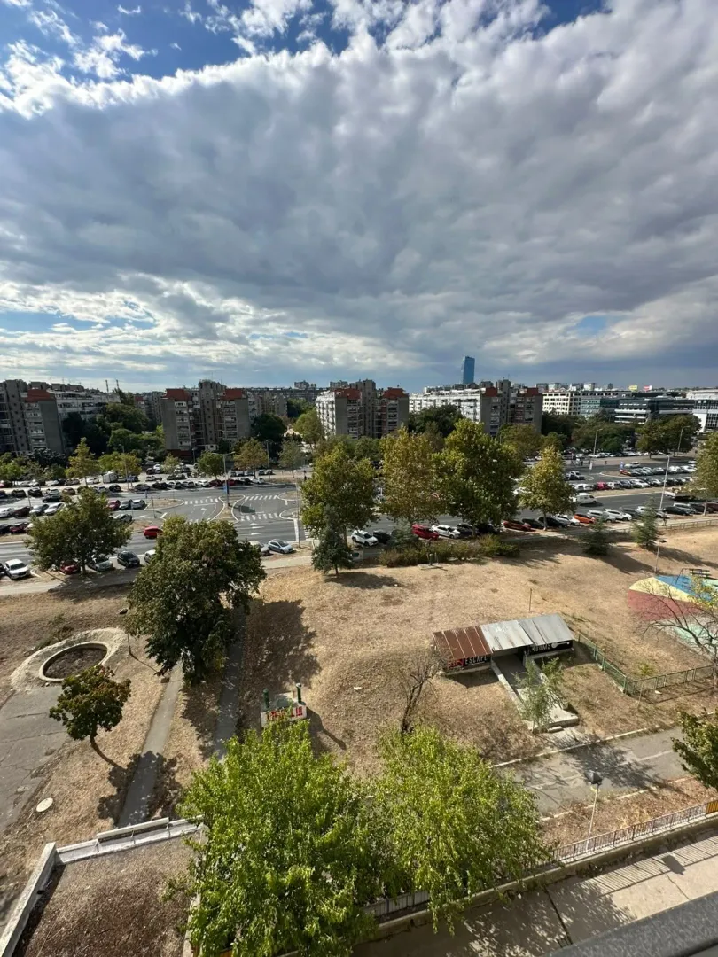 Pogled iz stana na gradsko područje sa ulicom i zelenilom.