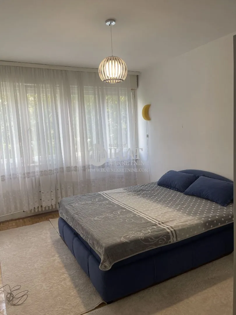 Bedroom with a double bed and a window with white curtains.