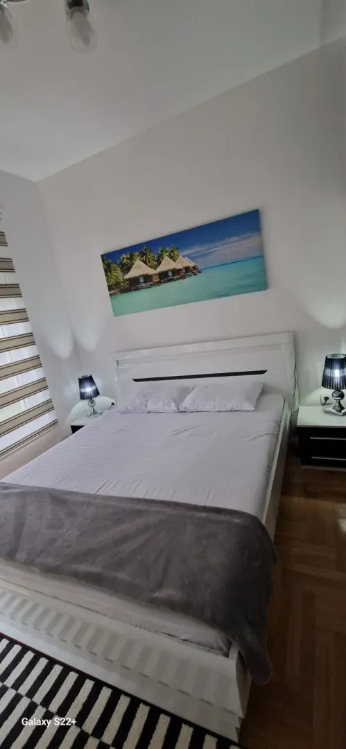 Bright bedroom with a large double bed, nightstands, and a wall painting.