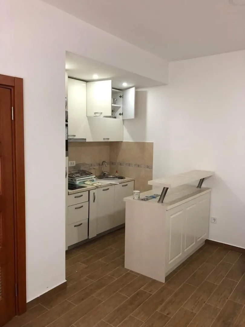 Small white kitchen with a bar counter and open upper cabinets.