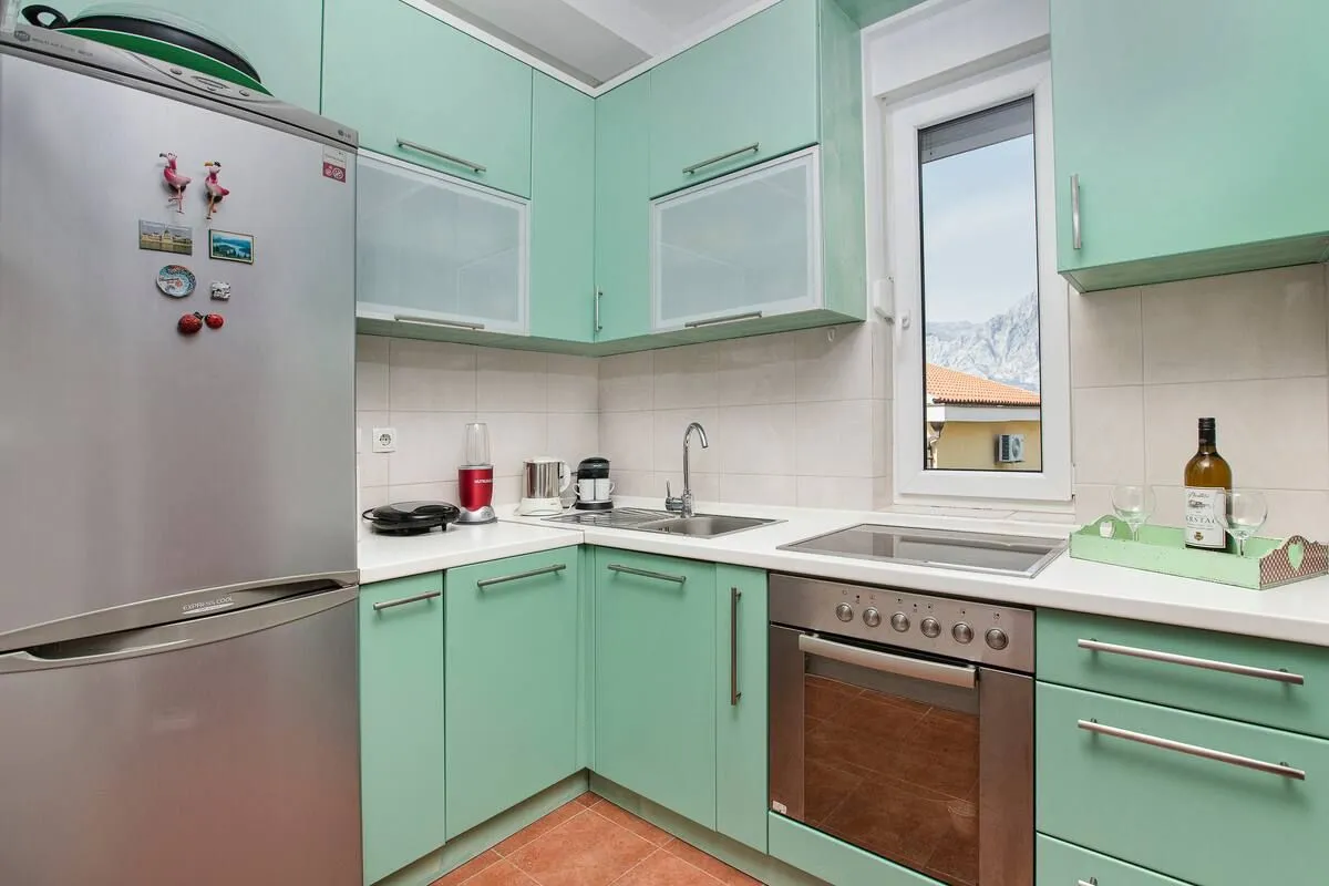 Kitchen in green tones with built-in appliances and a refrigerator.