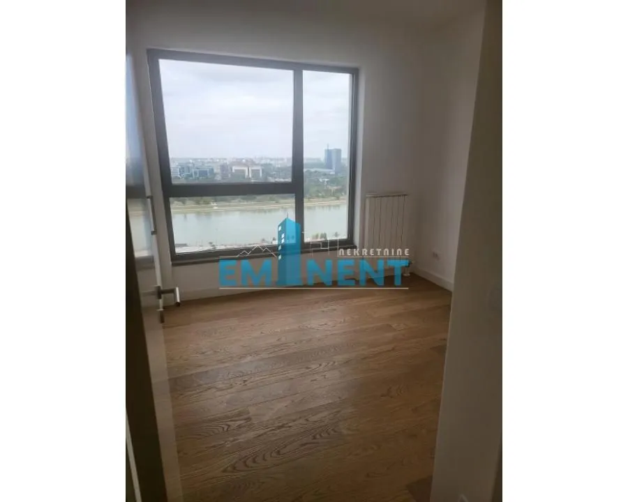 Empty room with wooden flooring and a large window overlooking the river.