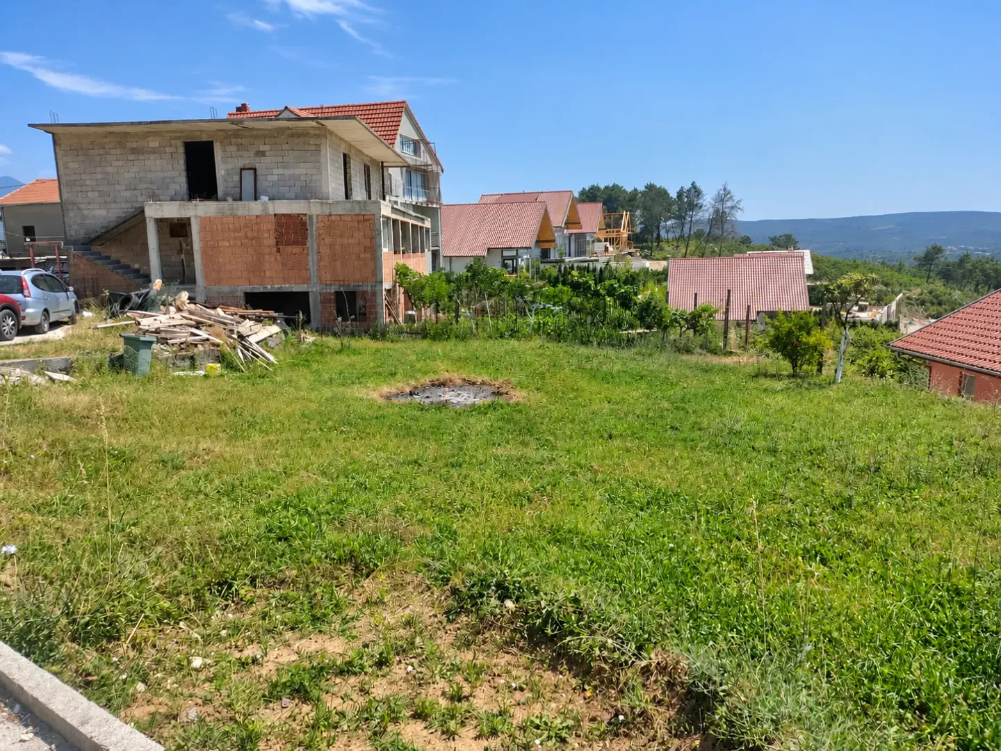 Pogled na porodičnu kuću u izgradnji sa dvorištem i okolnim kućama.