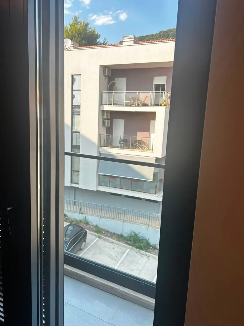 Pogled kroz prozor na susjednu zgradu i parking.