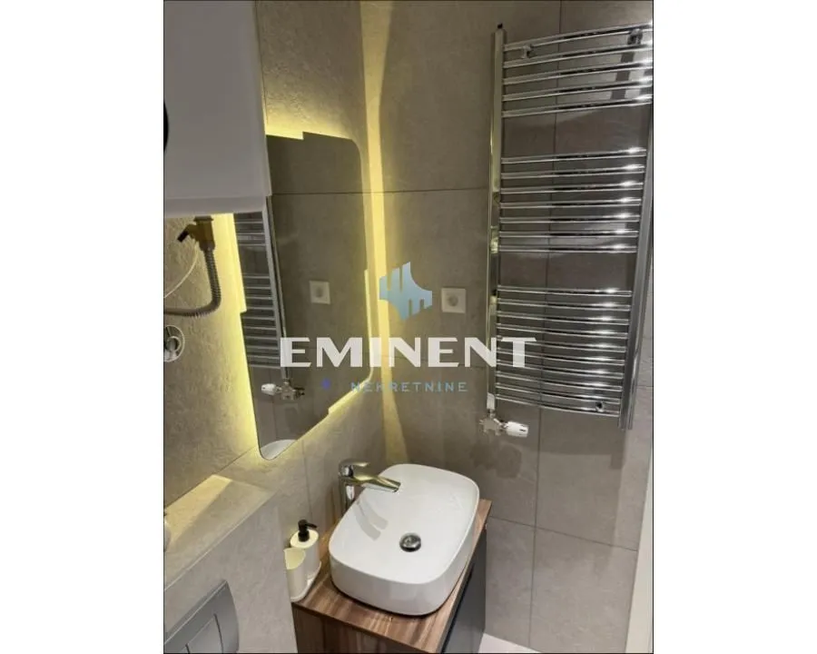 Modern bathroom with a basin, backlit mirror, and a towel rail.