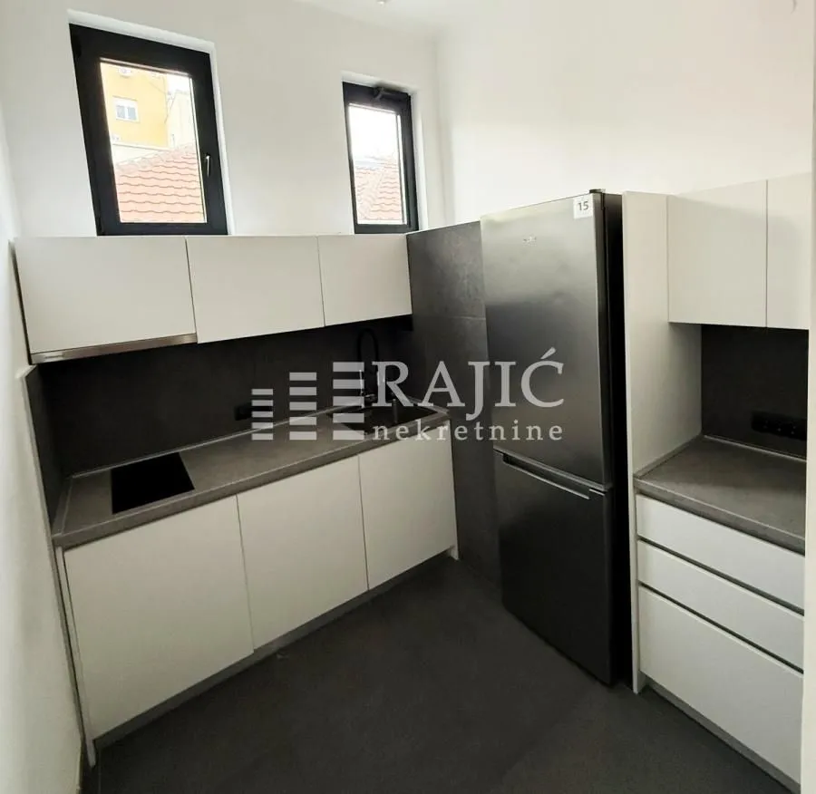 Modern white kitchen with dark countertops and a refrigerator.
