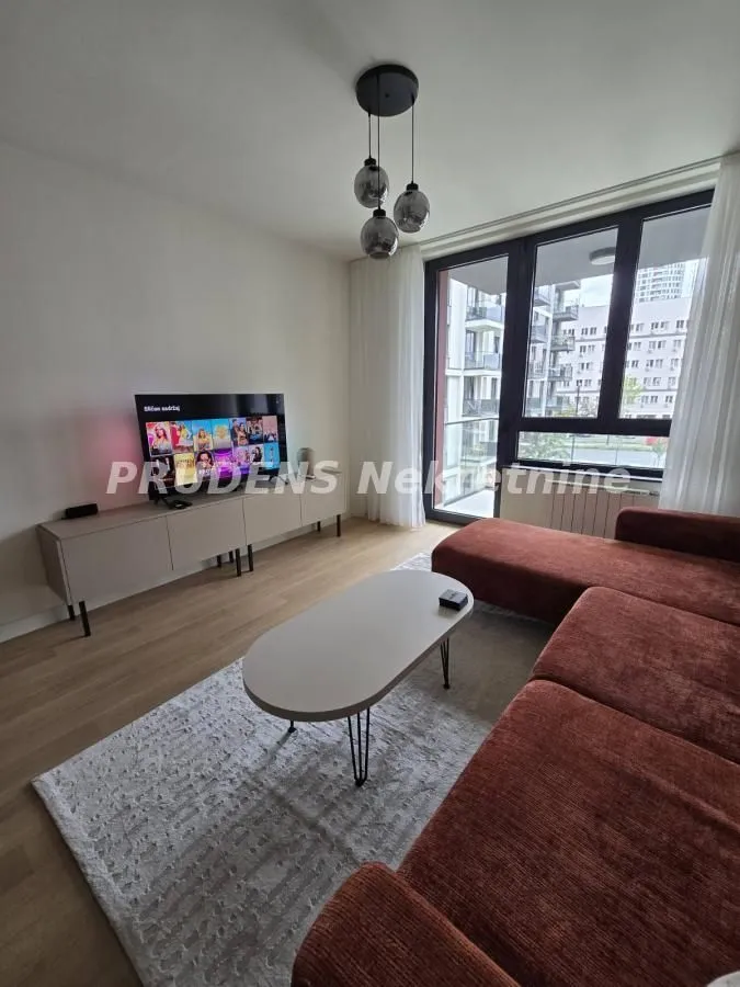 Dnevna soba opremljena ugaonom garniturom, TV-om i izlazom na balkon.