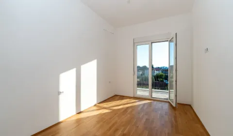 Prazna soba sa parketom i balkonskim vratima koja vode na terasu. - image 3
