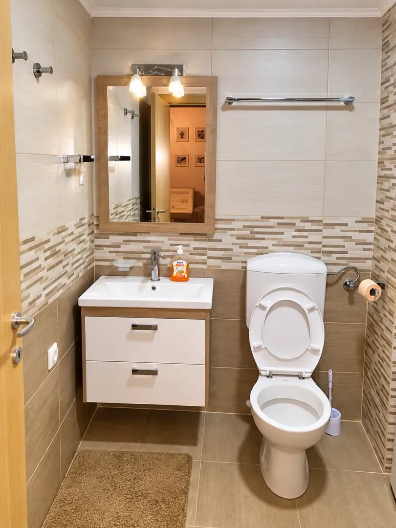 Compact bathroom with a sink, mirror, and toilet in beige tones.