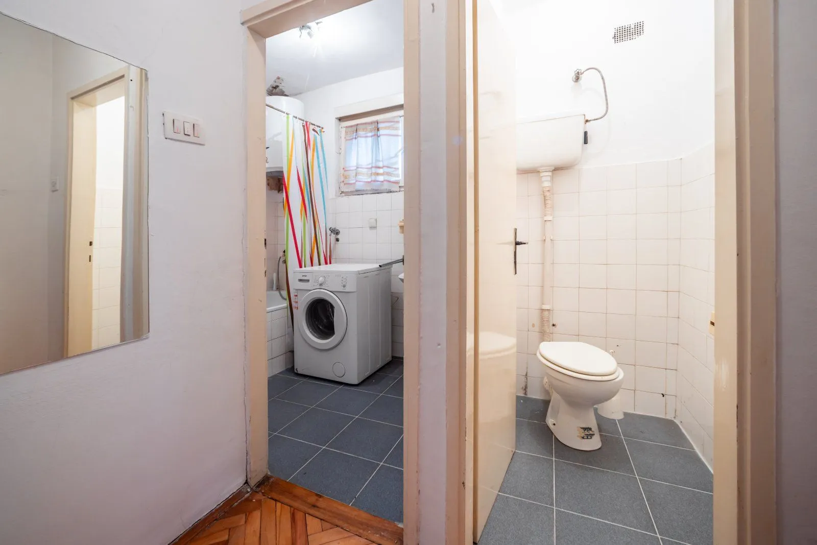 Pogled na kupatilo sa WC šoljom i veš mašinom.
