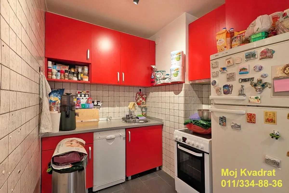 Manja kuhinja sa crvenim elementima i ugrađenim kućnim aparatima.