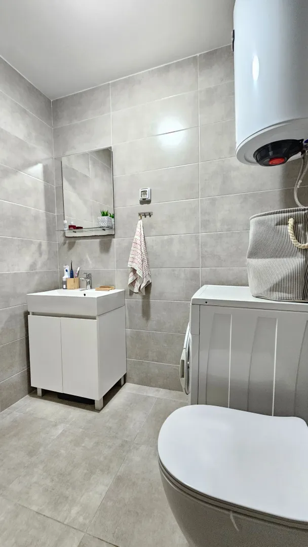 Modern and neatly equipped bathroom with a washbasin, toilet, washing machine, and water heater.