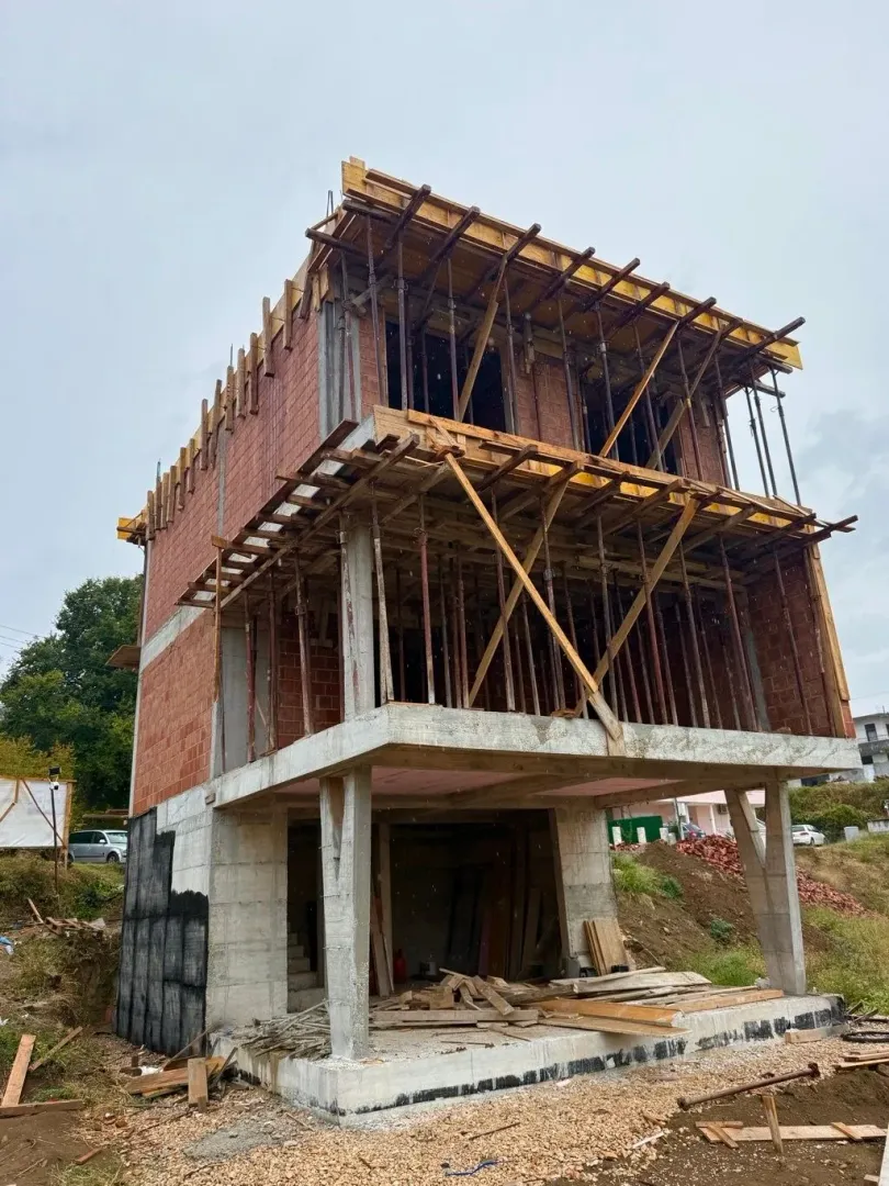 View of a family house under construction with visible concrete structure and bricks.