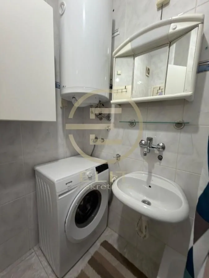 Manje kupatilo sa umivaonikom, veš mašinom i bojlerom na zidu.