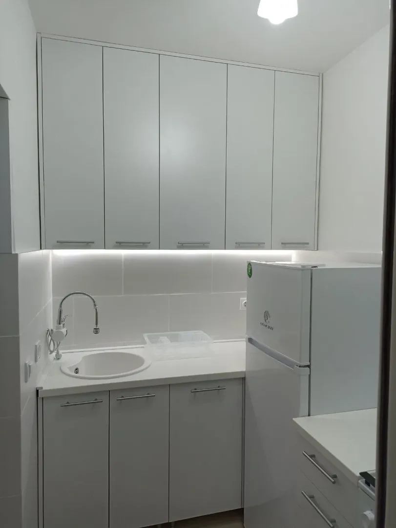 Bijela kuhinja sa sudoperom, radnom pločom i frižiderom.