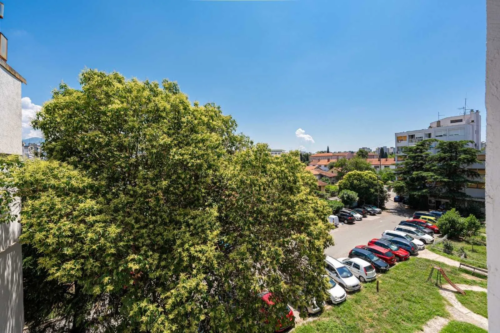 View from the terrace overlooking greenery and the parking lot in front of the building.