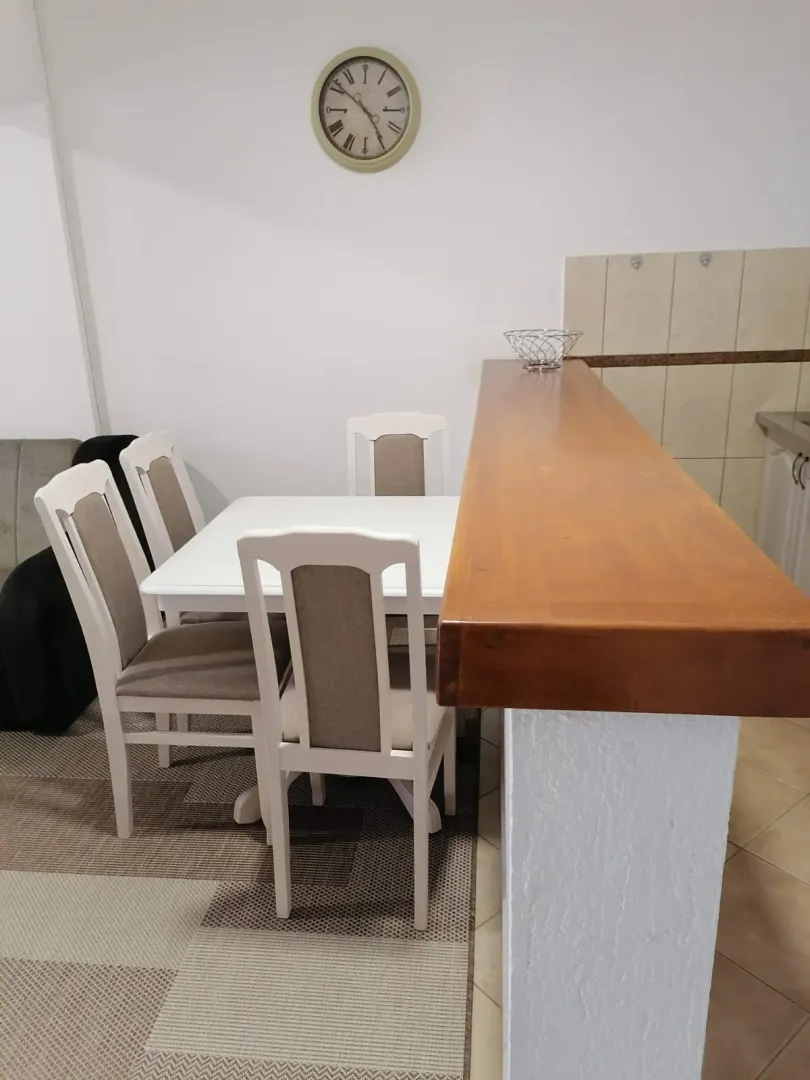 Trpezarija sa bijelim stolom i stolicama pored šank-pulta u kuhinji.
