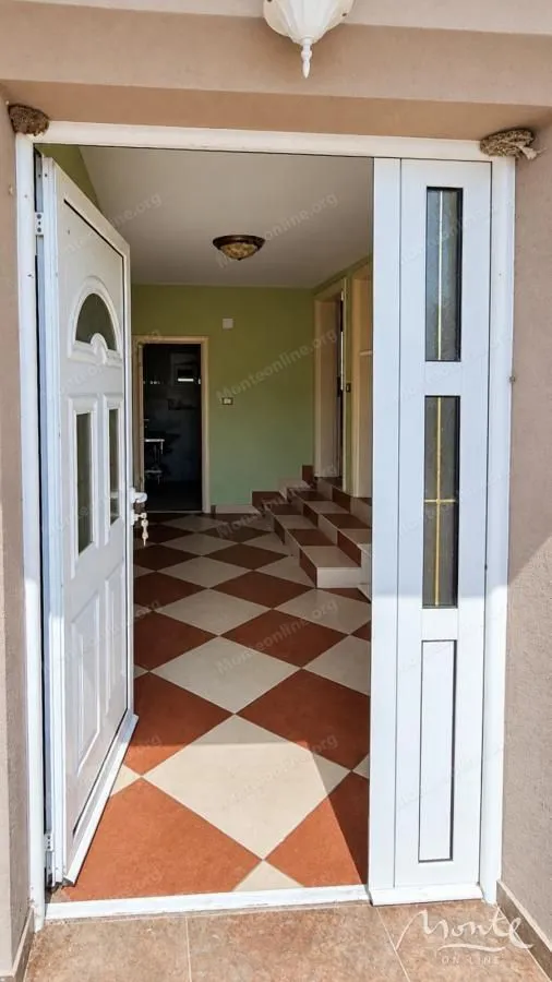 Pogled kroz otvoren ulaz u unutrašnjost kuće sa keramičkim pločicama na podu.