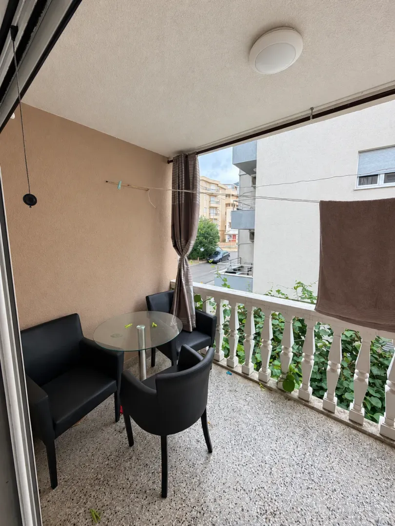 Covered balcony with seating furniture and a view of surrounding buildings.