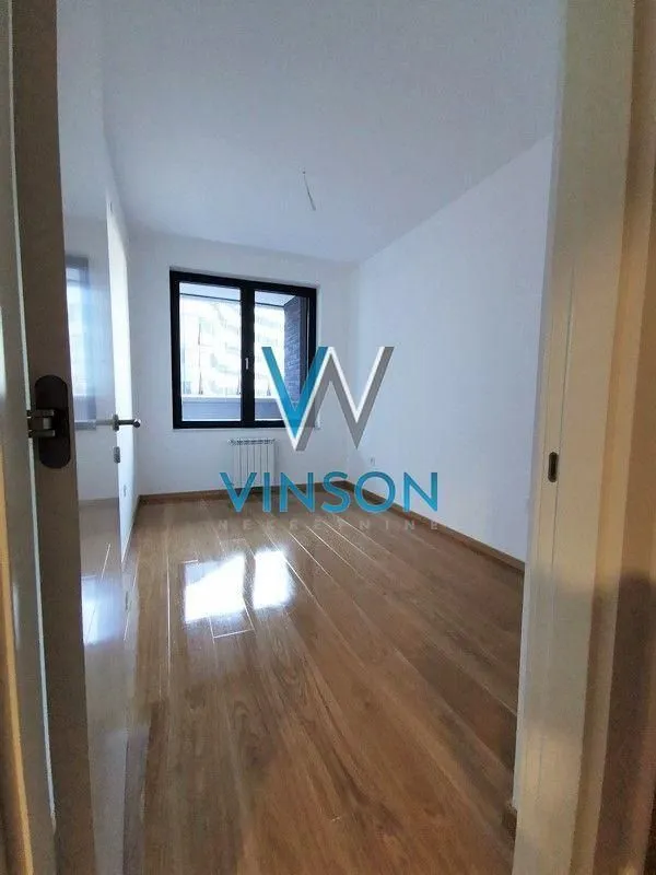 View from the hallway into an empty room with hardwood floors and a window.