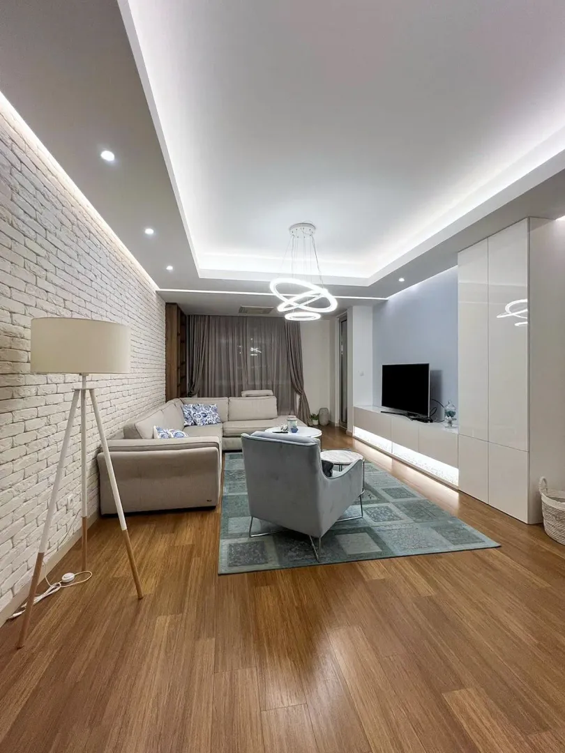 Moderan dnevni boravak sa ugaonom garniturom, TV komodom i spuštenim plafonom sa rasvjetom.