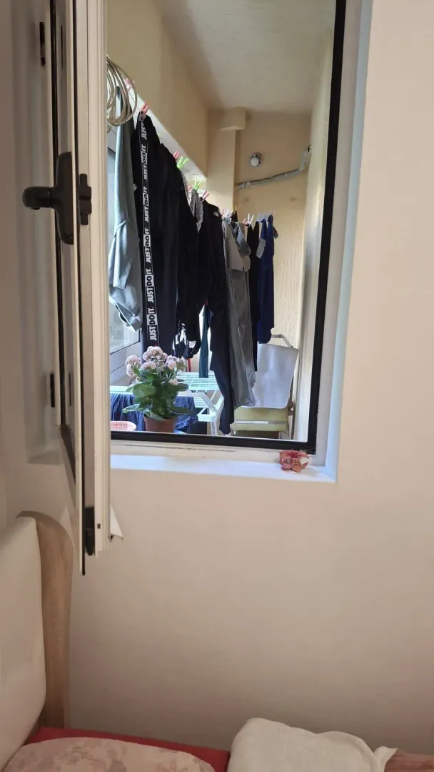Pogled kroz otvoreni prozor na balkon sa okačenim vešom.