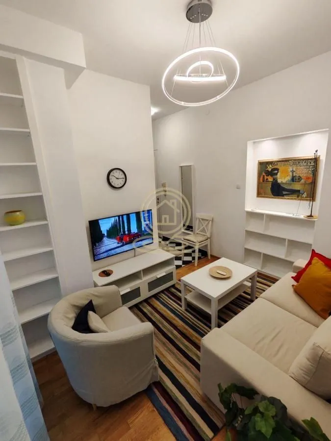 Small furnished living room with sofa, TV, and white shelving units.