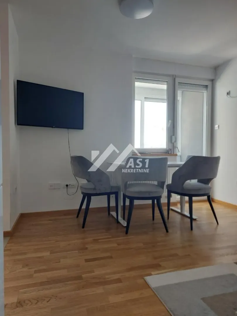 Dnevna soba sa trpezarijskim stolom, stolicama i televizorom na zidu.