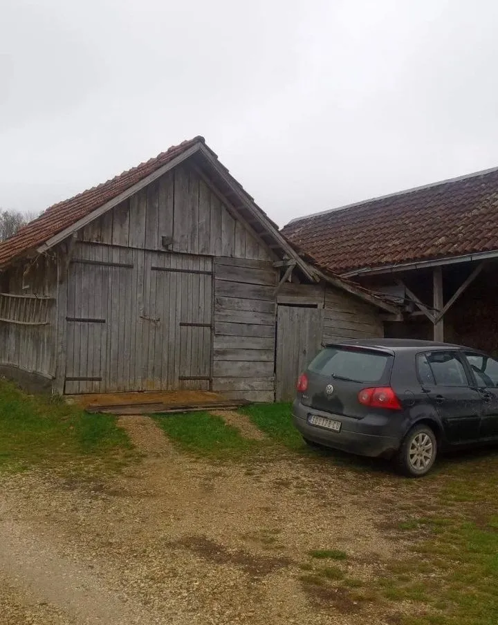 Pogled na drvenu pomoćnu zgradu sa dvorištem i parkiranim automobilom.