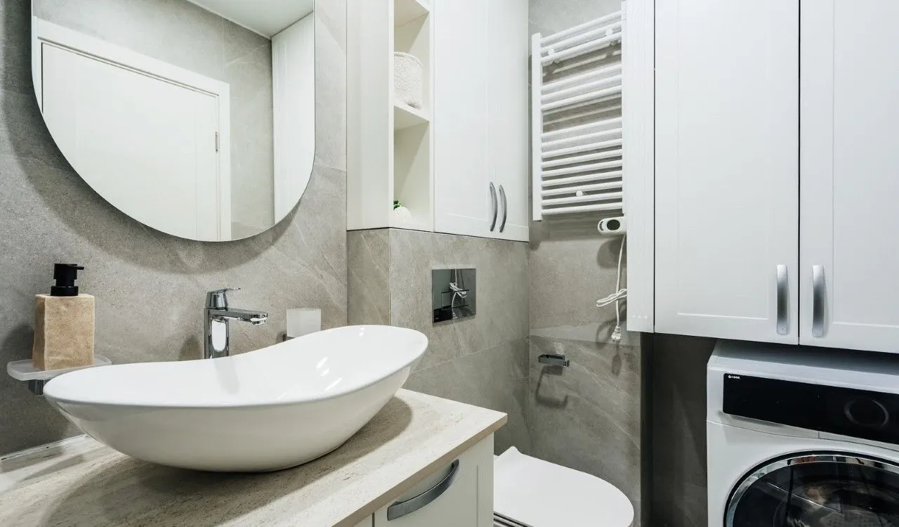 Modern bathroom with a sink, toilet, washing machine, and a mirror.