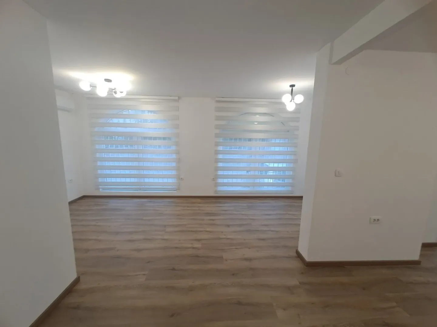 Empty spacious room with parquet flooring and windows with blinds.