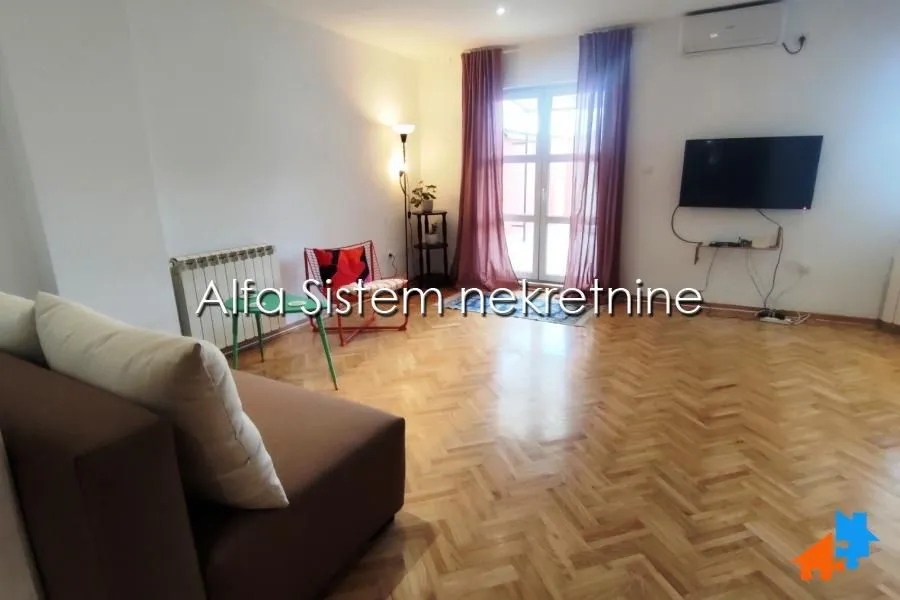 Living room with a sofa, TV, and wooden flooring.