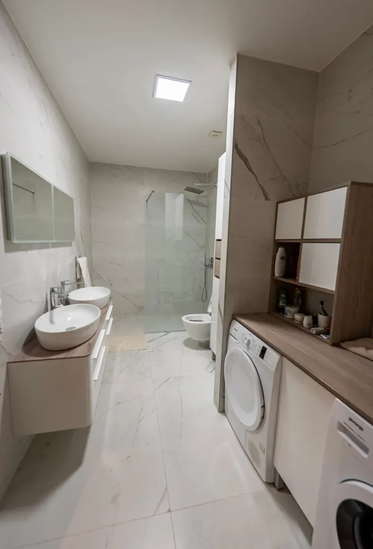 Modern bathroom with two sinks, a walk-in shower, and a washing machine.