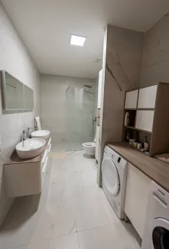 Modern bathroom with two sinks, a walk-in shower, and a washing machine. - image 9