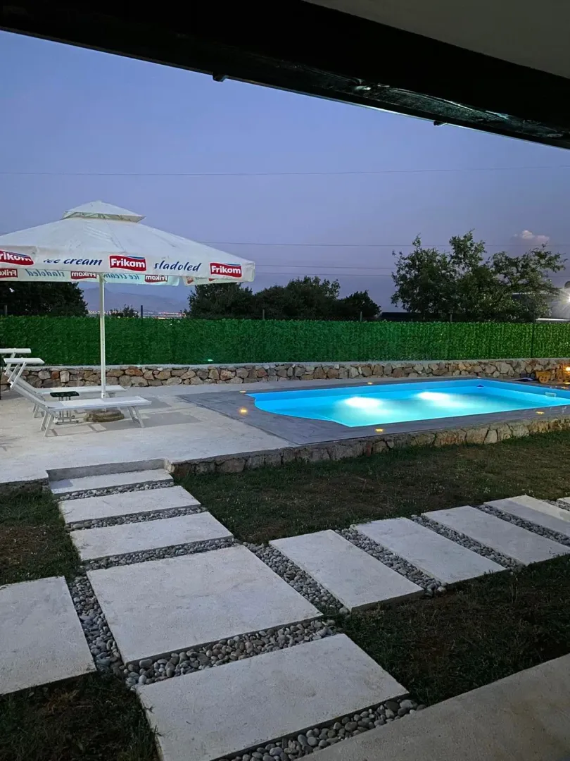 View of the courtyard with an illuminated swimming pool and sun loungers at dusk.