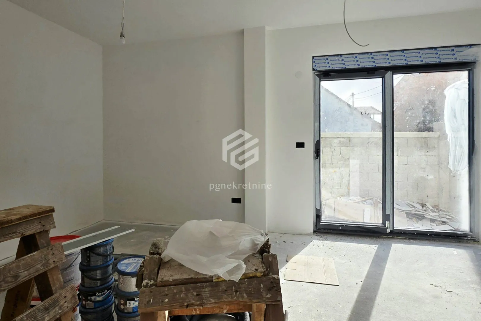 Nezavršena prostorija sa balkonskim vratima i građevinskim materijalom.