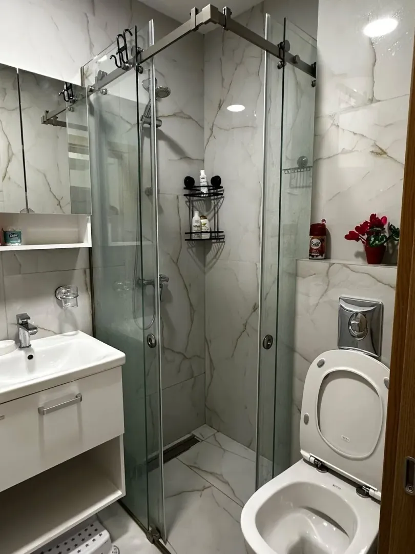 Moderne kupatilo sa tuš kabinom, umivaonikom i wc šoljom obloženo mermernim pločicama.