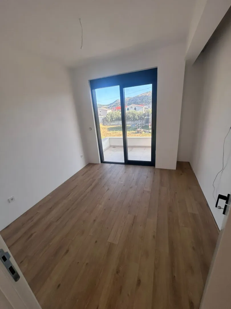 Prazna soba sa drvenim podom i izlazom na balkon.