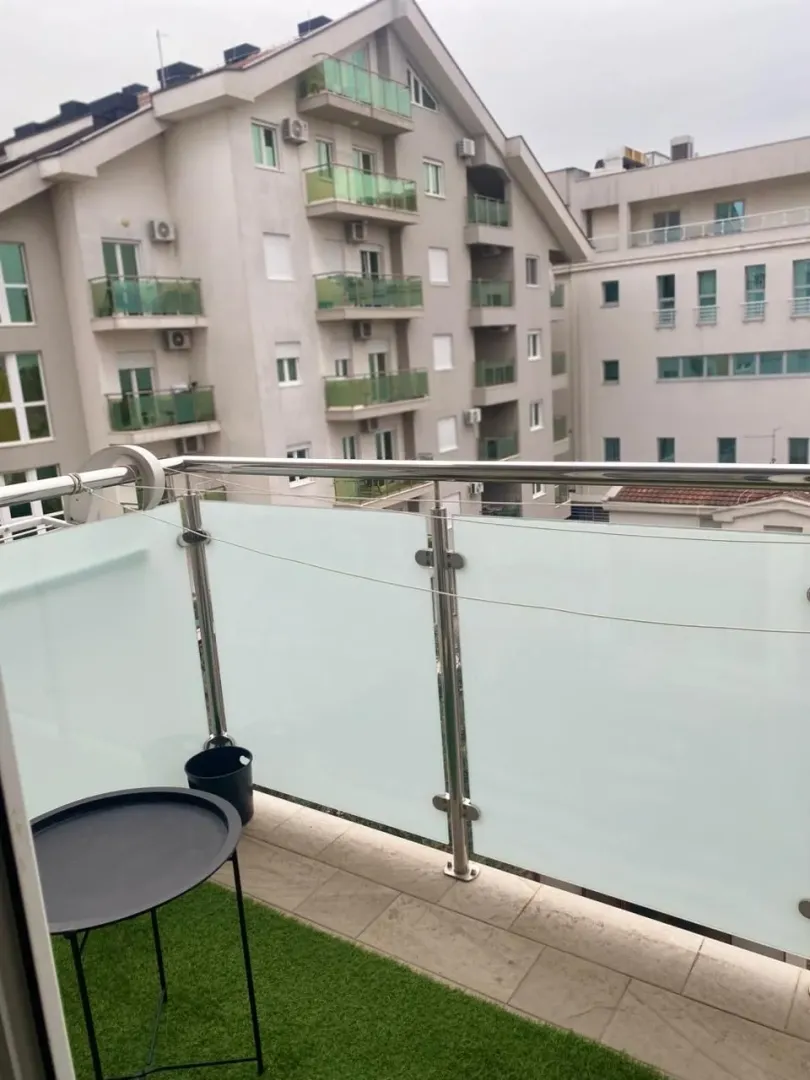 Manji balkon sa staklenom ogradom i pogledom na susjedne zgrade.