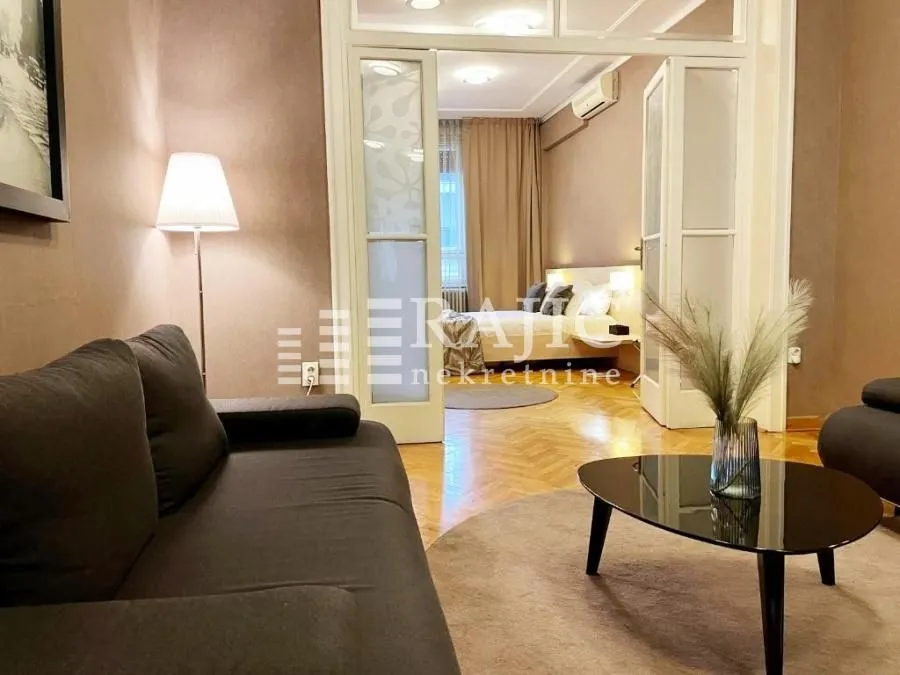Living room with a sofa and a view of the bedroom through glass doors.