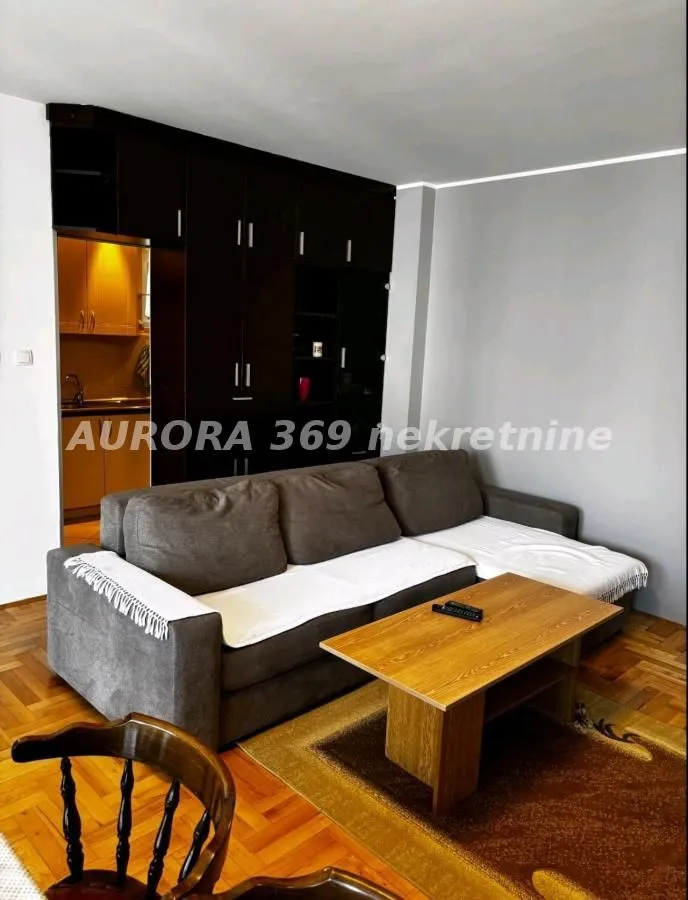 Dnevna soba sa ugaonom garniturom, drvenim stočićem i pogledom na kuhinju.