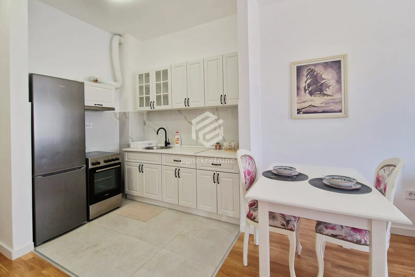 Small kitchen with white cabinets and a dining table on the right.
