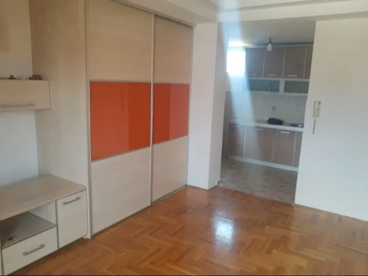 Soba sa ugradnim plakarom i kuhinjom u pozadini.
