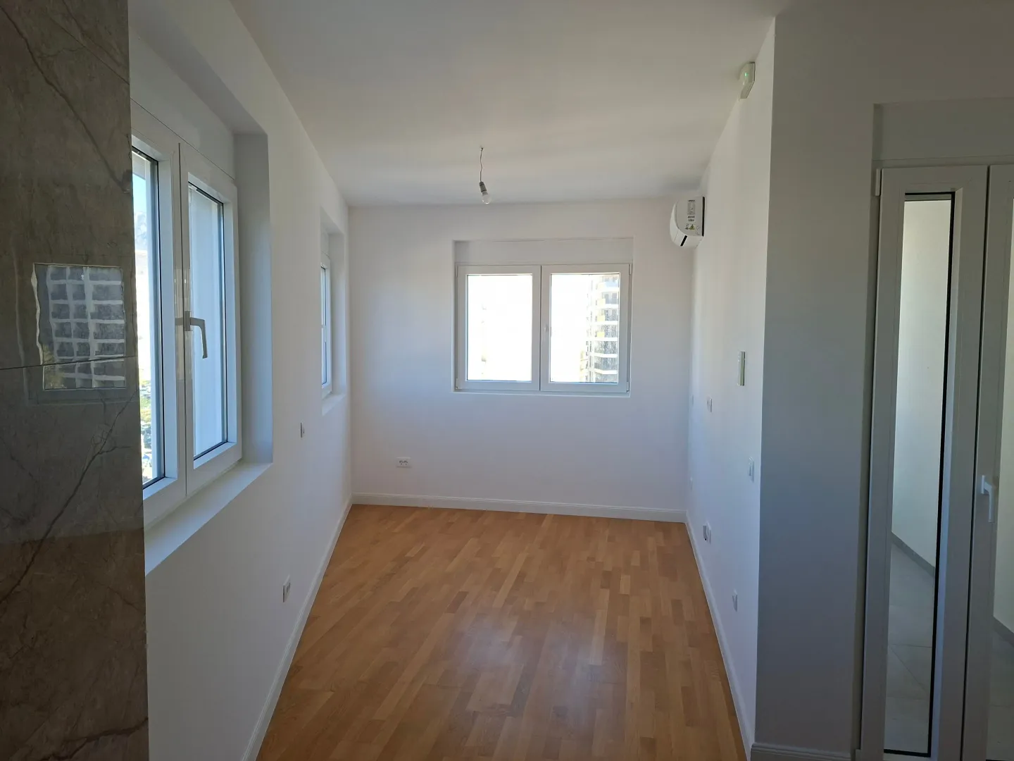 Empty bright room with parquet flooring and an air conditioner.