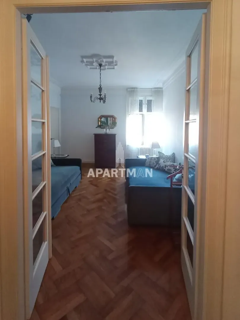 Pogled kroz vrata na dnevnu sobu sa garniturom i drvenim podom.