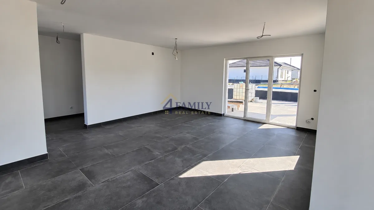 Empty room with dark floor tiles and glass doors leading outside.