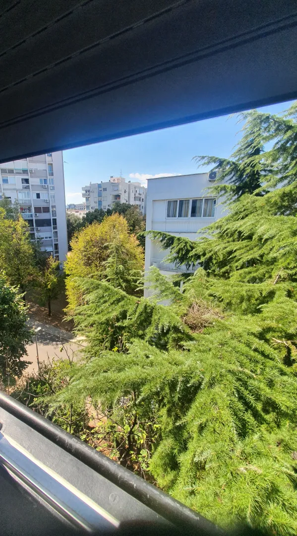 Pogled sa prozora na okolne zgrade i drveće.
